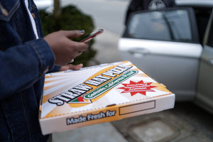 A customer carries a pizza box to their car