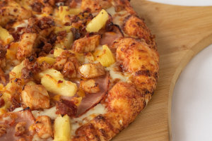 A close-up view of a pizza with ham, pineapple, bacon and chicken